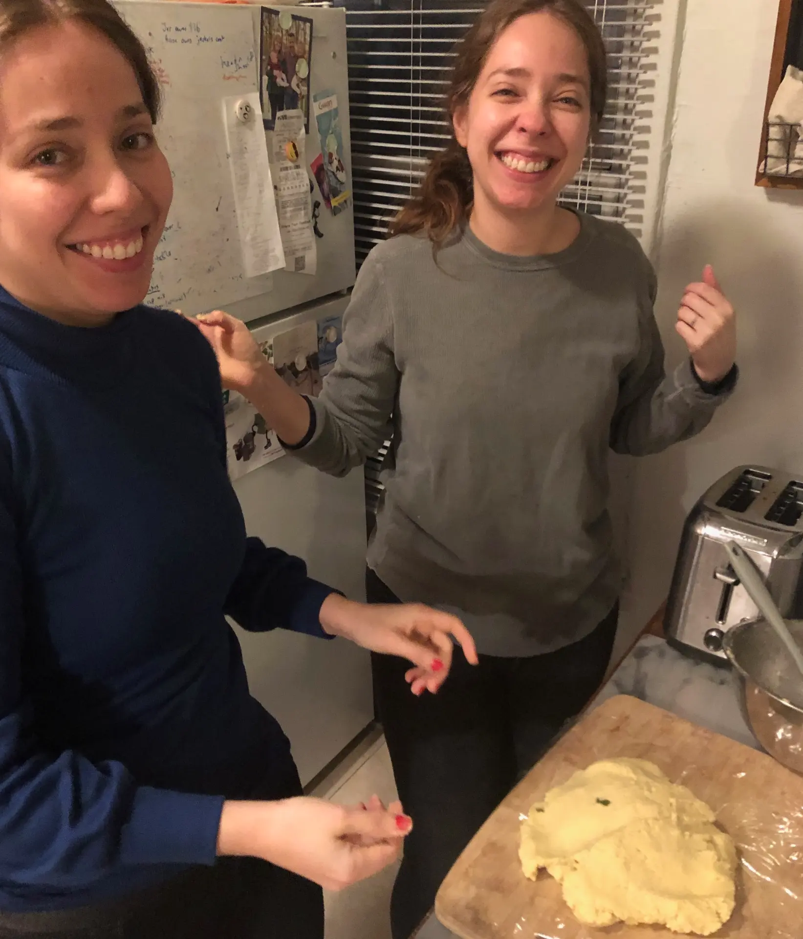 Two friends smiling in the kitchen with fresh dough on a cutting board