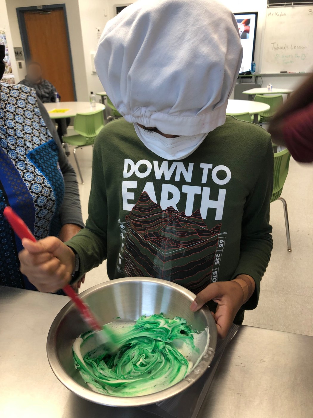 Student folding green-tinted frosting in a mixing bowl