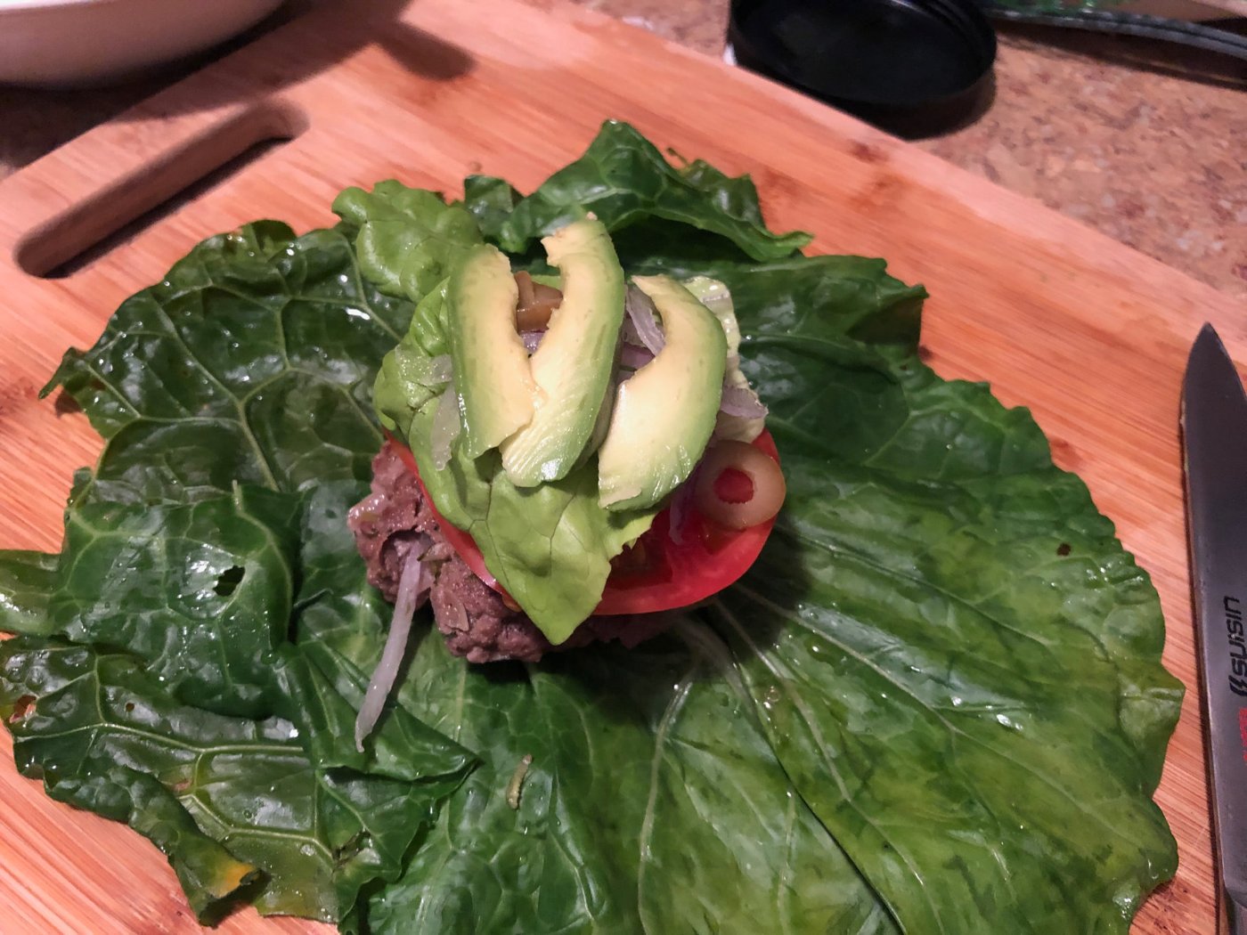 A burger wrapped in collard greens with avocado and tomato