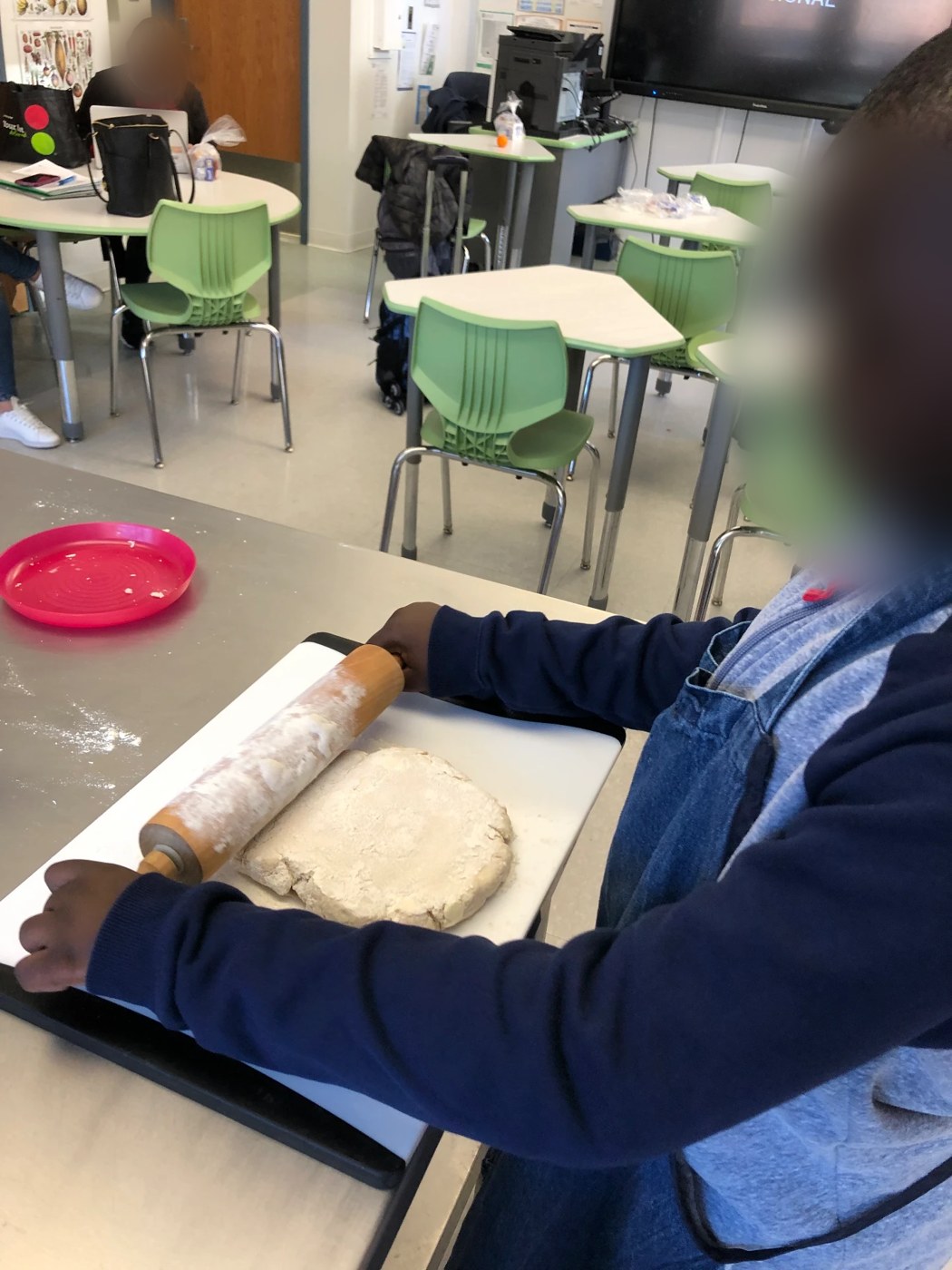 Student rolling out dough with a rolling pin in the classroom kitchen