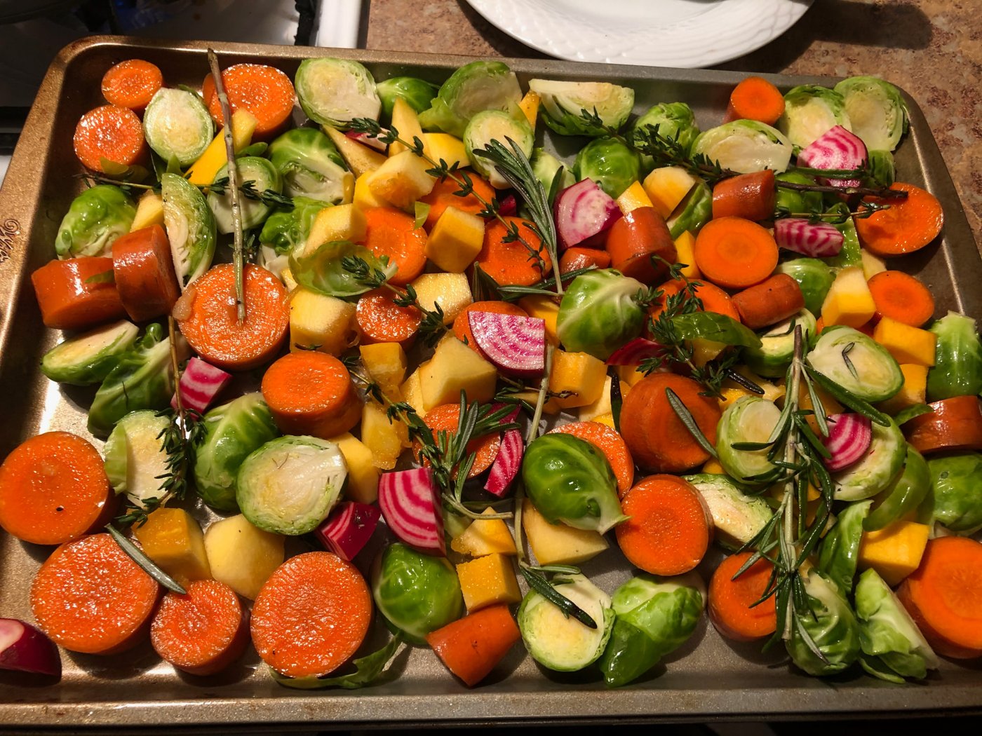 A sheet pan of seasoned carrots, brussels sprouts and squash ready to roast